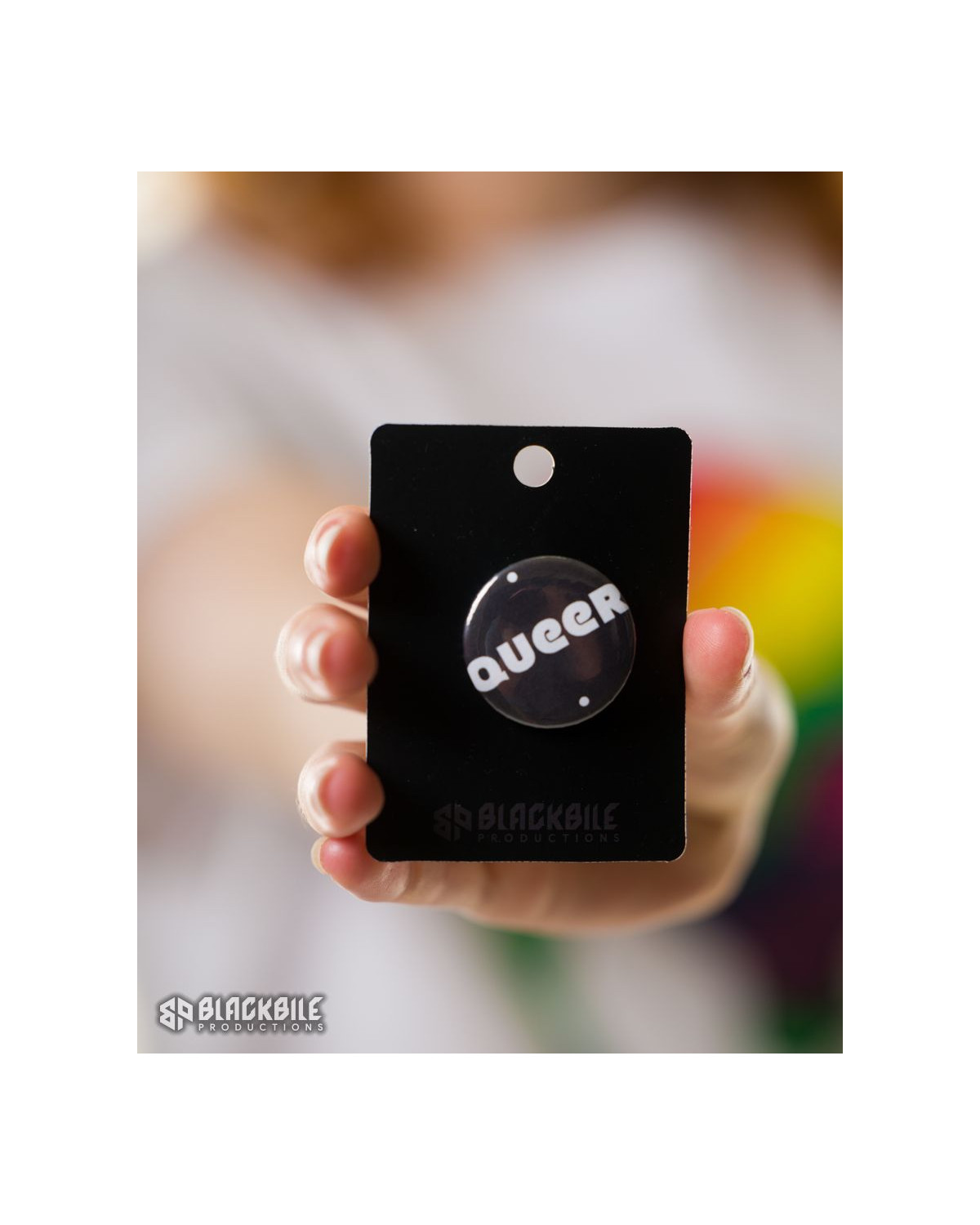 A small button badge in black colour with the word Queer in white.