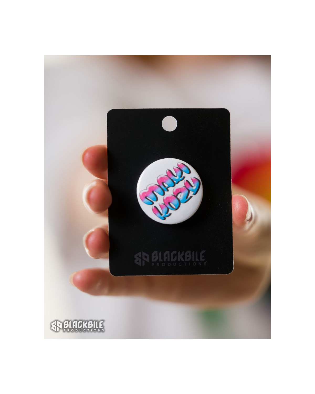 A small white button badge with the words Maxi Kozy – a quote from Dima Arrest in blue and pink colours.